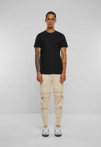 Svart t-skjorte med korte ermer, parret med beige cargo-bukser med glidelåslommer, akkompagnert av blå og hvite joggesko.