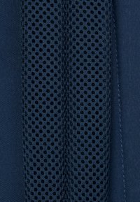 Tessuto blu navy con una sezione a rete con perforazioni circolari, bordata da un tessuto liscio su un lato e una cucitura texture sull'altro.