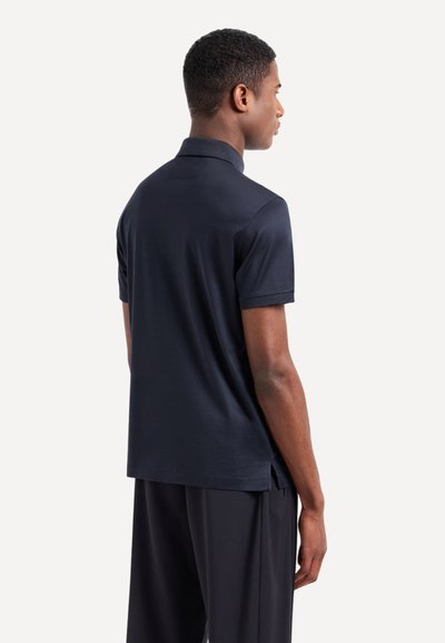 Polo shirt navy a maniche corte con colletto classico, texture morbida e spacchi laterali all'orlo per un facile movimento.