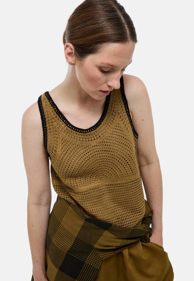 Débardeur en tricot couleur brun clair avec un motif texturé et des bordures noires, associé à un foulard à carreaux noué en vert foncé et noir.