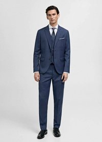 Un costume trois pièces bleu marine, ajusté, avec une veste à simple boutonnage, un pantalon assorti et une cravate à motif. Des chaussures noires complètent le look.