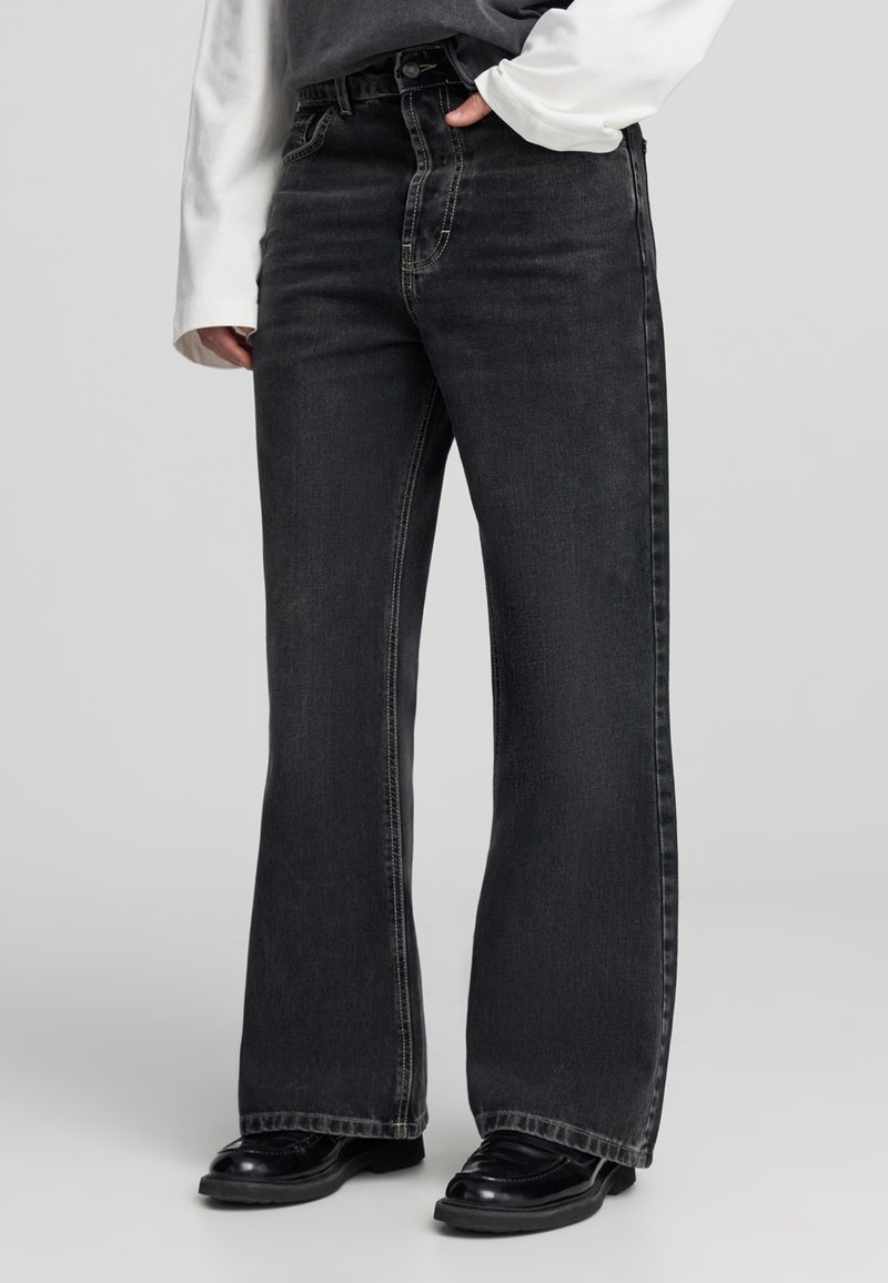 Jeans neri a gamba larga realizzati in denim, con vita alta, cuciture a contrasto e un classico design a cinque tasche.