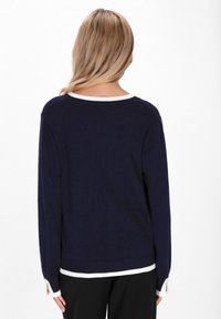 Pulover bleumarin cu mâneci lungi, manșete riburate și o margine albă în jurul decolteului și a tivului. Textură moale de tricot, croială casual.