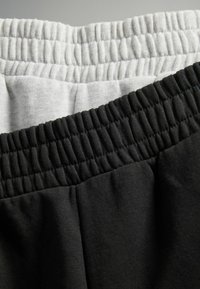 Twee paar joggingsbroeken samen getoond; de ene in lichtgrijs en de andere in zwart. Beide hebben elastische taillebanden en een zachte textuur.