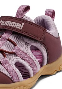 Fioletowy i purpurowy but sportowy z siateczkową cholewką, zapięciem na pasek, wygodną wkładką i gumową podeszwą. Posiada wentylowane wycięcia i teksturowane akcenty.