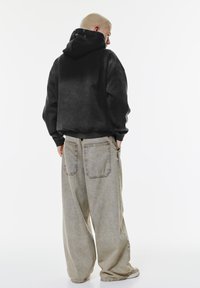 Felpa con cappuccio nera, dal tessuto a gradiente e vestibilità ampia, abbinata a pantaloni grigi chiari oversize con ampie tasche posteriori.