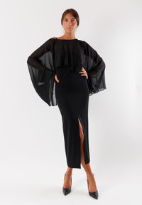 Lungo abito nero con una silhouette aderente e uno spacco alto alla coscia. Presenta maniche trasparenti e fluide con volants sovrapposti. Tessuto dalla texture liscia.
