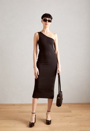 Black ribbed midi dress with one shoulder design, paired with black platform shoes and a small handbag. Smooth texture and fitted shape.