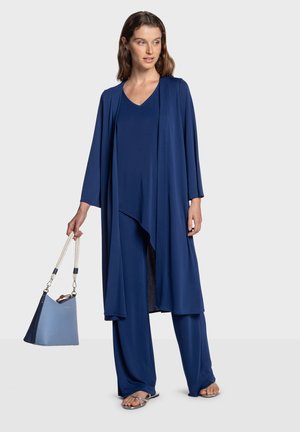 Tenue bleu marine aux manches larges et au design fluide, associée à un sac bleu clair. Le look est complété par des sandales plates argentées.