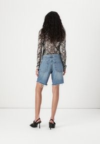 Shorts en denim avec un délavage bleu clair, ourlet effiloché et deux poches arrière, associés à un haut ajusté à manches longues avec un imprimé serpent.