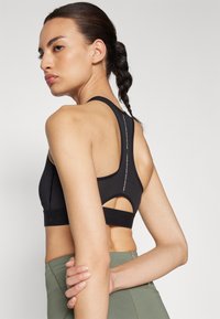Black sports bra featuring a racerback design and textured fabric. It has a cut-out detail at the back and a supportive waistband.