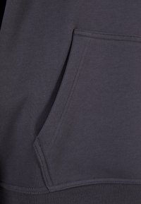 Tejido de sudadera gris con diseño de bolsillo tipo canguro, que presenta una textura suave y costuras resistentes a lo largo de las uniones y el dobladillo.