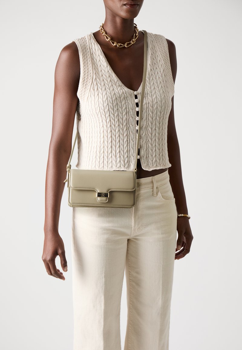 Gilet in maglia beige sopra una maglietta bianca, abbinato a pantaloni larghi beige. Una borsa a tracolla verde chiaro con una chiusura dorata in evidenza.