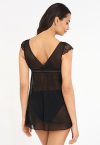 Vestido corto de tela negra transparente con mangas de encaje y diseño de espalda en V. Tiene una cintura ajustada y una falda suelta y fluida.