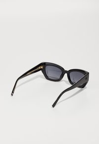 Black sunglasses with a geometric frame, dark lenses, sleek temples, and gold accents on the hinges, featuring a textured design.