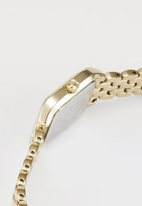 Montre en métal doré avec un boîtier rectangulaire, surface lisse et brillante, et bracelet à maillons. Présente une couronne pour l'ajustement et un design minimaliste.