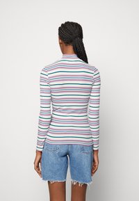 Chemise à manches longues à rayures dans des tons pastel, avec une texture côtelée, un col haut et une coupe ajustée, associée à un short en jean effiloché.