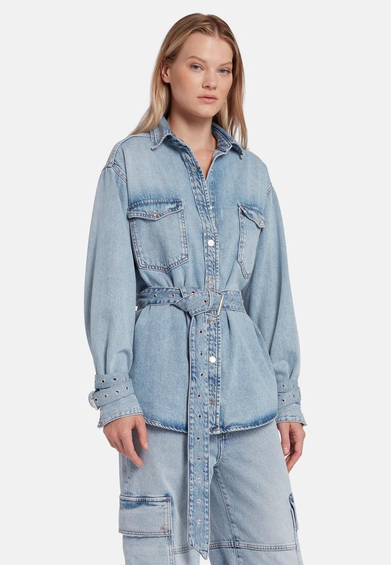 Lichtblauw denim overhemd met lange mouwen, riem in de taille, twee borstzakken en oogjes-detail op de mouwen. Zacht, licht vervaagd materiaal.