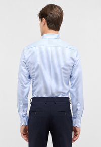 Blauw-wit gestreepte overhemdead met lange mouwen en knoopmanchetten, gecombineerd met navy broeken met twee achterzakken en knoopdetails.