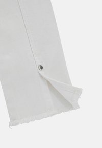 Tessuto di denim bianco con orlo sfrangiato e dettaglio con bottone a pressione argentato. Il materiale è testurizzato e presenta un design pulito.