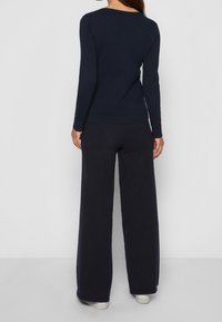 Haut bleu marine à manches longues avec un col rond, associé à un pantalon ample bleu marine, tous deux en tissu doux. Chaussures décontractées visibles.