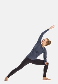 Long-sleeve, gray athletic top with a fitted design, paired with black leggings. The figure is in a yoga pose, stretching one arm upward.