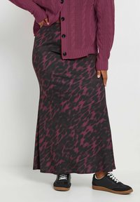 Jupe maxi noire avec un motif abstrait multicolore bordeaux, associée à un cardigan en tricot torsadé et des baskets noires, blanches et à semelle en caoutchouc.