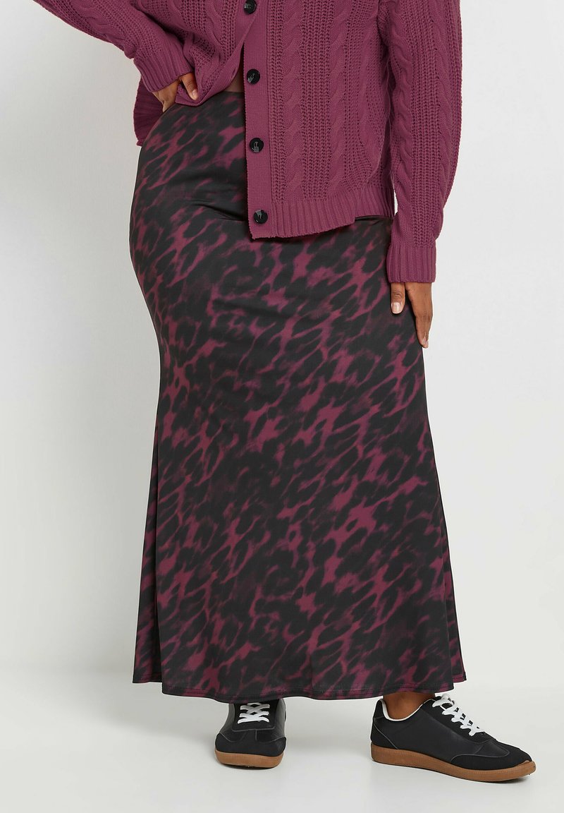Jupe maxi noire avec un motif abstrait multicolore bordeaux, associée à un cardigan en tricot torsadé et des baskets noires, blanches et à semelle en caoutchouc.