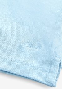 Telar de algodón azul claro con una textura. Presenta un logo cosido en un tono más claro y una costura ordenada a lo largo del dobladillo y los bordes.