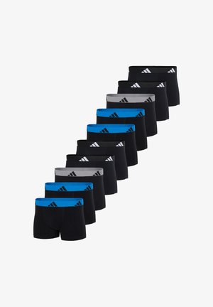 Athletischer Mann steht barfuß da, trägt schwarze Boxer-Shorts mit einem blauen Bund und Adidas-Logo vor einem schlichten weißen Hintergrund.