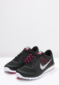 Zapatos deportivos negros con parte superior de malla, que presentan un patrón de acento rosa y un logo de swoosh de Nike en blanco. Suela de goma con buena tracción.