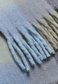 Uldhalstørklæde i gradient nuancer af blå og beige med teksturerede frynser i varierende tykkelse og blødhed.