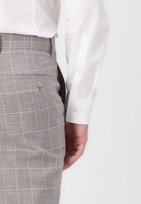 Hellgraue Leinenhose mit Karomuster, ausgestattet mit einer Seitentasche und einem dezenten Knopfdetail, kombiniert mit einem weißen Langarmhemd.