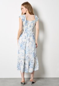 Robe midi florale en bleu clair et blanc, avec un corsage smocké, des manches volantées et un ourlet fluide. Tissu lisse et léger.