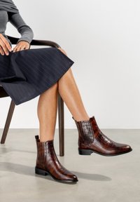Braune, krokodilpräge Lederankelstiefel mit runder Zehenform und niedrigem Blockabsatz, ausgestattet mit seitlichen elastischen Einsätzen und einem eleganten Design.
