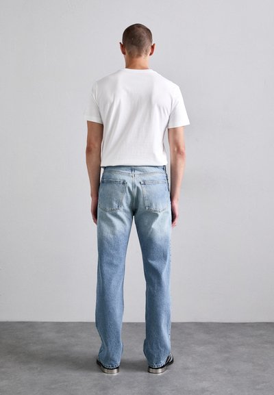 Vit kortärmad t-shirt och blekta blå raka jeans. Jeans har bakfickor och en ljus tvätt med subtil gradient.