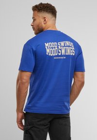 Blå bomulds T-shirt med "MOOD SWINGS" trykt tydeligt i hvid på ryggen, kortærmet og med rund halsudskæring.
