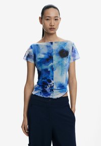 Blusa con motivo ad acquarello blu, maniche corte e scollatura off-shoulder; tessuto morbido e semitrasparente; design a strati.