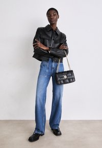 Black leather cropped jacket with buttons, light blue wide-leg jeans, and a black quilted handbag with a chain strap. Flat black shoes.