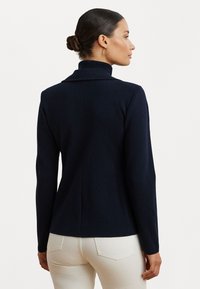 Temno modra dolgesleeve polo jopica z visokim ovratnikom in gladko teksturo, ki se ponaša s prilega obliko in detajlom šiva na hrbtu.