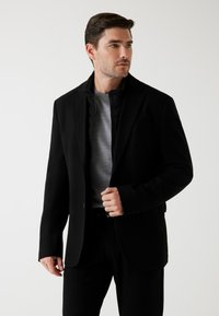 Zwarte blazer over een grijze trui, met een strak ontwerp, een soepele textuur en een aansluitende snit met een enkele knoopsluiting.