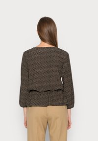 Blusa preta com padrão floral, com mangas longas e um design em camadas na barra. Tecido suave com um corte descontraído.