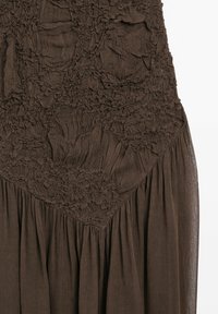Braunes Kleid aus strukturiertem Stoff mit verstreuten Rüschendetails und einem fließenden Rock. Der obere Abschnitt hat eine Diamantform mit gerafften Akzenten.