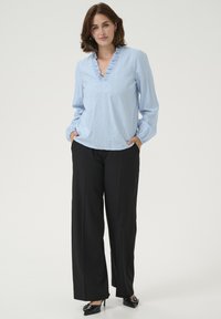 Light blue blouse with a ruffled v-neck, paired with black wide-leg trousers and black heels. Smooth fabric, relaxed fit.