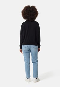Schwarzer Strickpullover mit langen Ärmeln und geripptem Saum. Hellblaue Slim-Fit-Jeans mit Gesäßtaschen. Weiße Sneakers runden das Outfit ab.