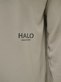 Beżowa fakturowana tkanina z małymi powtarzającymi się dziurkami oraz czarnym nadrukiem "HALO 196819721981" na ubraniu.