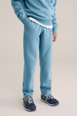 Ljusblåa sweatpants i ett mjukt tyg med avslappnad passform, med sidofickor och subtil logotyp på höften. Matchas med mörka sneakers.