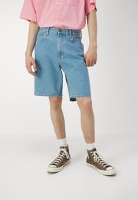 Ljusblå denimshorts, knälånga, med en klassisk femfickdesign och rak passform. Kombinerade med bruna högställda sneakers och vita strumpor.