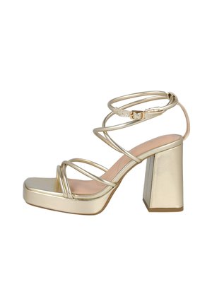 Sandal de tacón alto dorado con tiras, tacón cuadrado, punta cuadrada y hebilla ajustable en el tobillo sobre un fondo blanco.