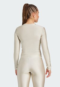 Dopasowany top z długim rękawem i legginsy z metalicznego beżowego materiału. Gładka tekstura z żebrowanym wykończeniem wzdłuż szwów.